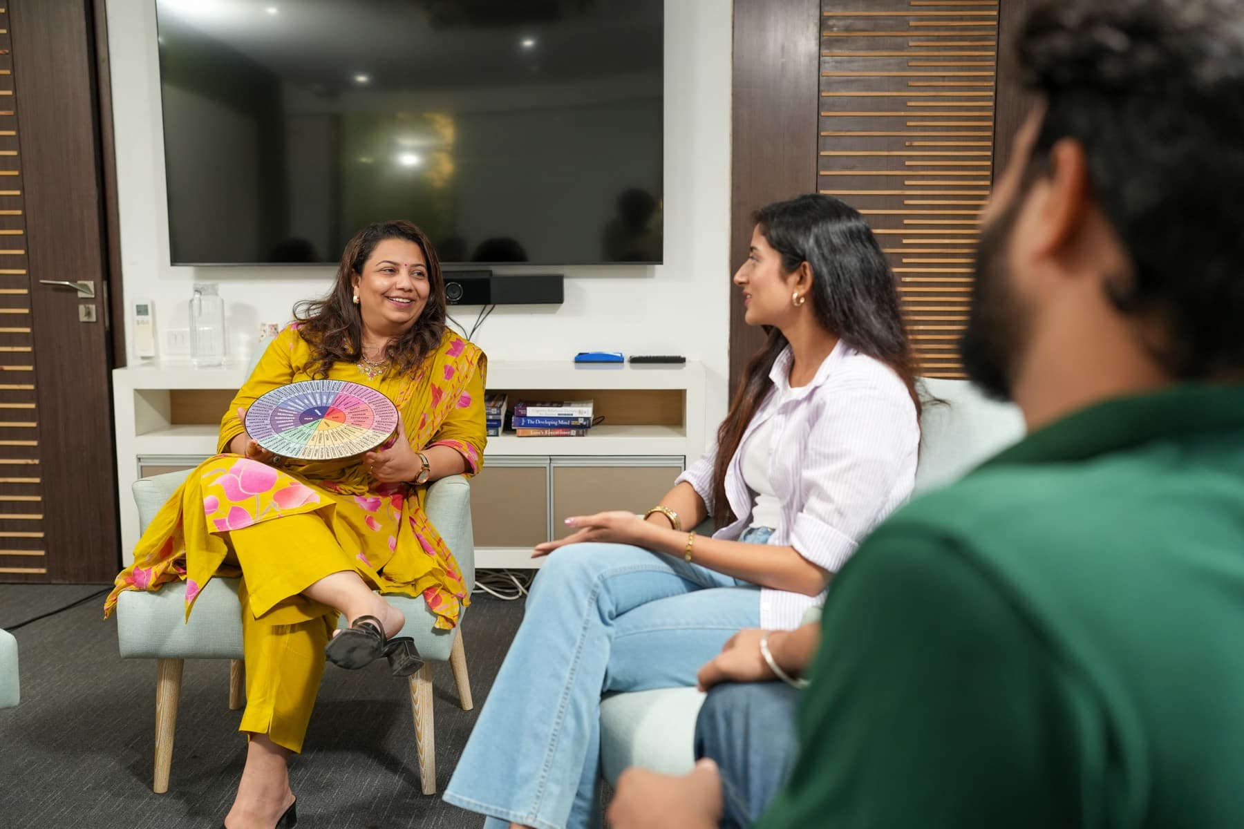 A Samarpan group facilitator holding a feelings wheel as participants listen.